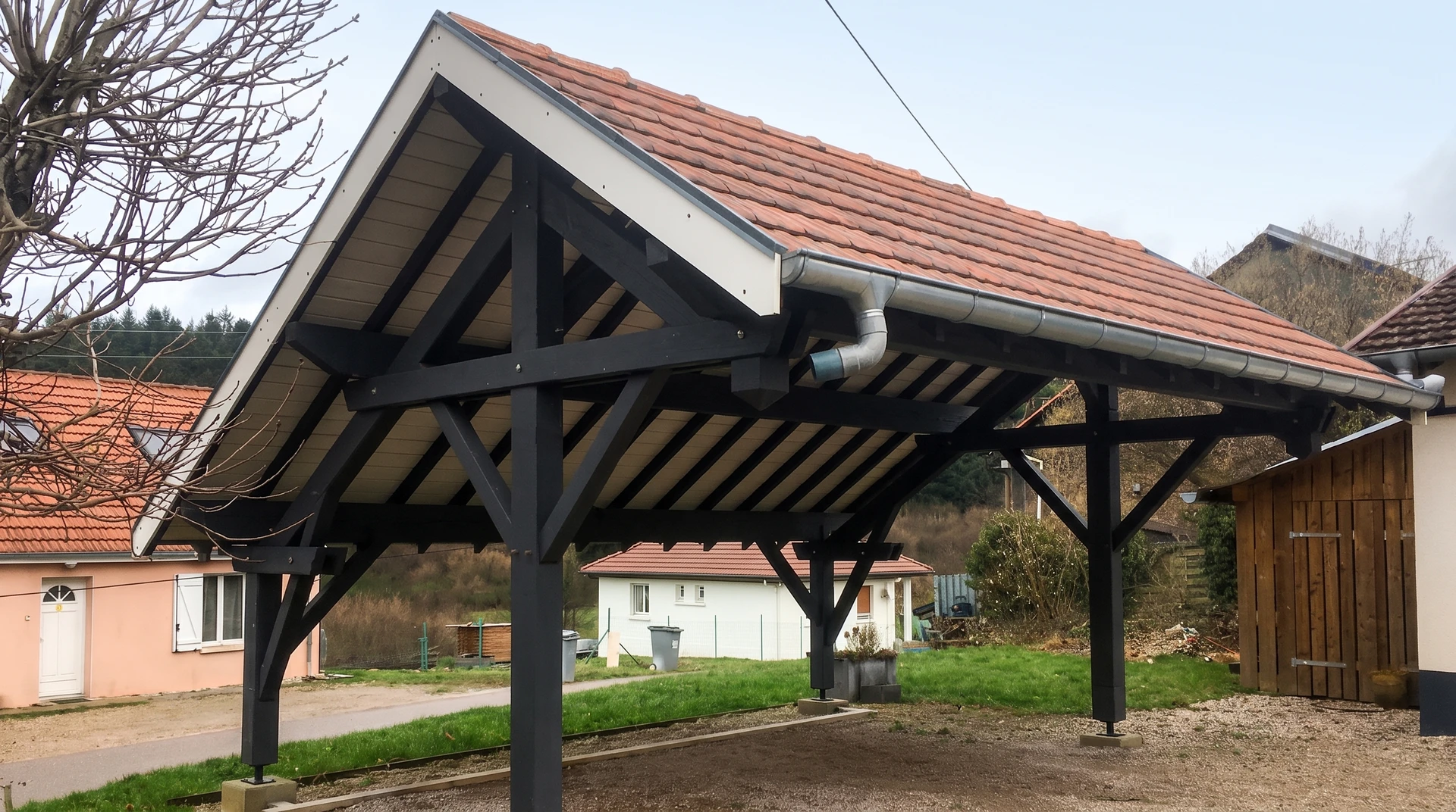 Carport en bois lamellé-collé teinte anthracite, structure à deux poteaux doubles avec contreventements diagonaux